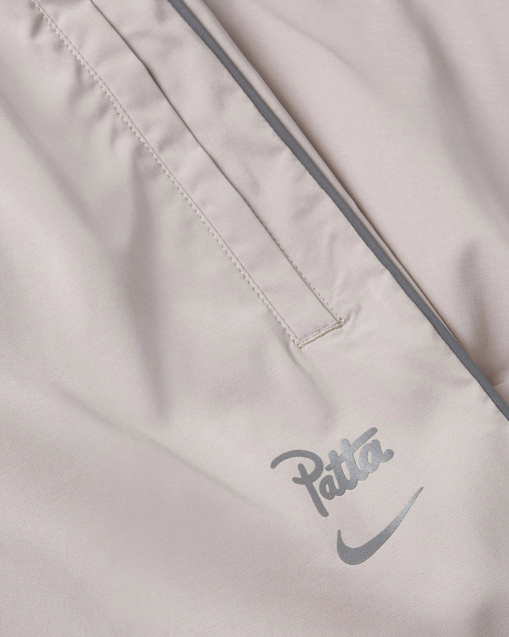 Close-up of Nike x Patta track pants in Sanddrift showing reflective branding and pocket detail.